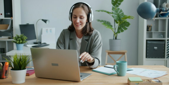 Woman wearing headphones works on a laptop at desk.
